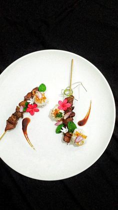 two small pieces of meat on skewers sitting on a white plate with flowers