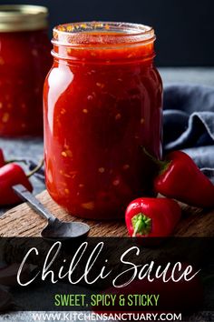 two jars filled with chili sauce sitting on top of a cutting board next to spoons