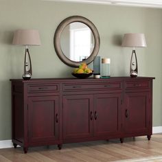 a sideboard with two lamps and a bowl of fruit on it in front of a mirror