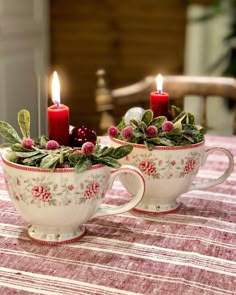 two tea cups with holly and berries on them, one is lit by the candle