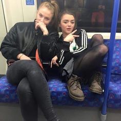 two young women sitting on a subway train looking at the camera and pointing their fingers