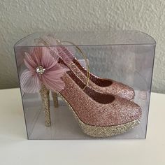 a pair of pink high heeled shoes with a flower on the side in a clear box