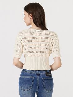 a woman in jeans and a sweater is looking down at her back while she's wearing