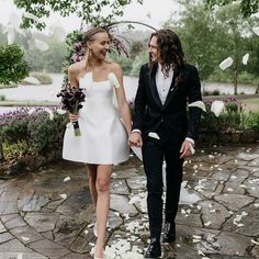 a man and woman holding hands while walking down a path with petals on the ground