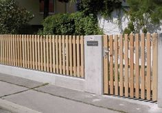 a wooden fence on the side of a street next to a sidewalk with trees and bushes behind it