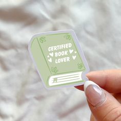 a hand holding a book shaped sticker with the words certified book lover on it