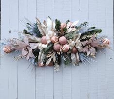 a christmas wreath hanging on the side of a white wooden wall with pink and gold ornaments