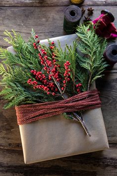 a wrapped present with red berries and greenery tied to it on a wooden table