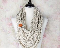 a white mannequin with a brown button on it's neck and a beige knitted scarf