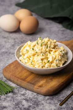 an egg salad in a bowl on a cutting board next to eggs