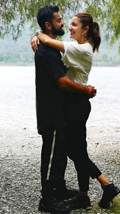 a man and woman hugging under a tree by the water