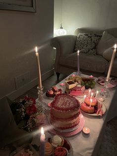 a table topped with cakes and candles next to a couch in a room filled with furniture