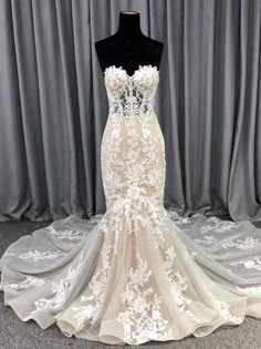 a white wedding dress on display in front of grey curtained backdrop with sheer drapes