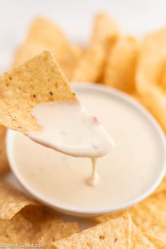 a tortilla chip being dipped with ranch dip from a white bowl filled with chips