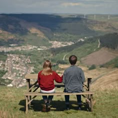 two people sitting on a bench looking out over the valley and town in the distance