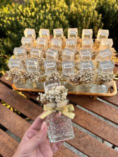 a person holding up a glass bottle with flowers in it on a wooden table outside