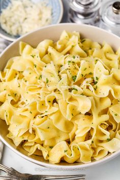 a white bowl filled with pasta on top of a table next to silverware and utensils