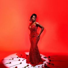 a woman in a red dress standing against a red background with roses on the floor