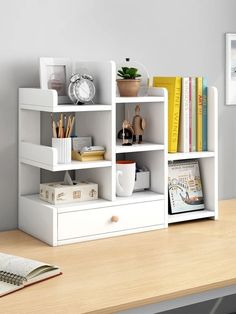 a white book shelf with books, magazines and other items on it next to a desk