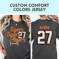 Show your team spirit with this custom Comfort Colors tshirt perfect for GAME DAY! Customize not only your color, but your school name, and player number. :)  HOW TO ORDER SHIRTS 1. REVIEW ALL PHOTOS for size and color options, as well as shop policy. 2. CHOOSE SHIRT SIZE from the drop-down menu. Notice the size guidance graphic if you want the trendy oversized look.  3. CHOOSE SHIRT COLOR from drop-down menu. 4. INSERT PERSONALIZATION 5. ADD TO CART (If ordering multiples, repeat steps 2-5) 6. CHECKOUT after carefully reviewing your cart. We welcome questions so please don't hesitate to send us a note.  PRODUCT MATERIAL DETAILS: Comfort Colors garments UNISEX and are made 100% with ring-spun cotton. The soft-washed, garment-dyed fabric brings extra coziness to your wardrobe while the rela Customizable Crew Neck T-shirt For Fan Gear, Collegiate T-shirt With Custom Print For Game Day, Custom Print T-shirt For Sports Events, Customizable T-shirt For Football Season, Collegiate T-shirt With Name Print For Fans, Varsity T-shirt With Team Name For College, Customizable Casual T-shirt For Cheerleading, Custom Print Crew Neck T-shirt For Game Day, Team-colored Crew Neck T-shirt For Cheerleading