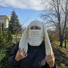 a woman wearing a white knitted hat and scarf with her hands in front of her face