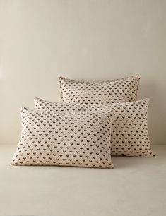 three pillows on a bed with white wall in the background and light colored flooring