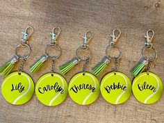 tennis ball keychains with name tags and tassels attached to them on a wooden surface