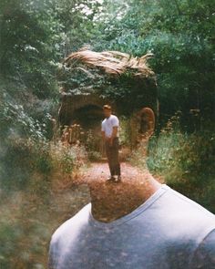 a man standing in the middle of a forest next to a large head with trees on it