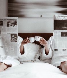 a woman laying in bed holding a coffee cup and reading the paper on her side