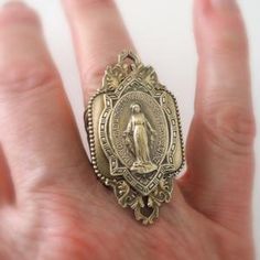 a person's hand holding a gold ring with an image of the virgin mary on it