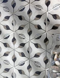 a glass vase filled with rocks next to a tile wall covered in black and white leaves