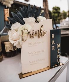 there is a sign that says drinks on it and flowers in front of the sign