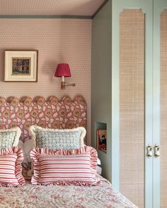 a bed with pink and white pillows in a bedroom next to a wallpapered headboard