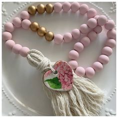 a white plate topped with pink beads and tasseled necklace next to a gold bead