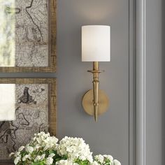 a vase with white flowers sitting on a table next to a wall mounted mirror and lamp