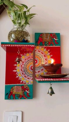 two red and green wall hangings with an elephant design on them, next to a potted plant