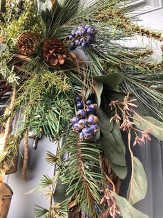 a wreath with pine cones, berries and evergreen leaves hanging from the side of a door