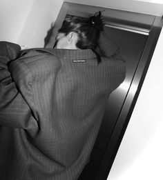 a woman in a suit leaning against a wall with her head on the door handle