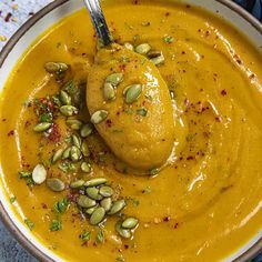 a bowl filled with yellow soup and topped with a ladle full of pumpkin sauce