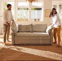 a man and woman standing in a living room next to a couch with pillows on it