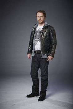 a man in a leather jacket and jeans posing for a photo with his hands in his pockets