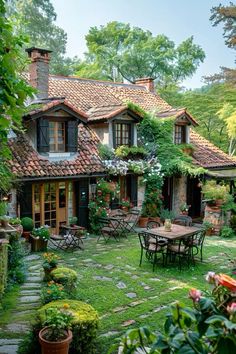 an outdoor patio with tables and chairs in front of a house surrounded by greenery