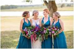 three bridesmaids in blue dresses holding bouquets and smiling at each other while standing under a tree