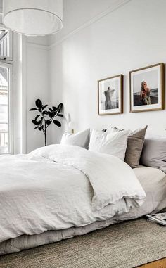 a bed with white sheets and pillows in a bedroom next to a window, framed pictures on the wall