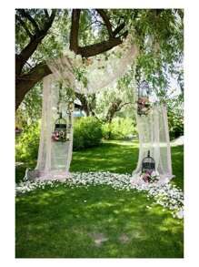 an outdoor wedding ceremony setup with white drapes and flowers on the grass, surrounded by trees