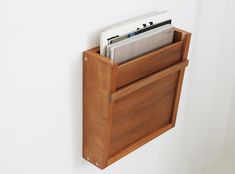 a wooden magazine holder holds magazines and folders in it's slot on the wall