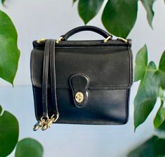 NAME OF BAG: Coach Willis MATERIALS: thick but supple and smooth leather, all metal is brass. COLOR: black COUNTRY of manufacture: China DATE of manufacture: 2001 CREED NUMBER: H13-9927 SIZE: medium capacity, 10.5" wide X 10.5" high X 3.5" deep. POCKETS: large zippered pocket inside across the back. Also slip pockets on the outside, under the front flap and on the back.  CLOSURE: brass turnlock STRAP: A top handle (2.5" drop) plus a detachable  crossbody strap, 44" long including the hardware (a drop of 22"). The strap is a vintage black leather strap from another vintage Coach bag with the exact same hardware as the original strap. I purchased the strap as a replacement for this bag's lost strap. CONDITION: A-, no tears, scratches, or stains on the bag outside, Almost perfect inside. No v Coach Willis, Vintage Coach Bag, Vintage Coach Bags, Coach Bag, Coach Leather, Vintage Coach, Brass Color, Crossbody Strap, Cloth Bags