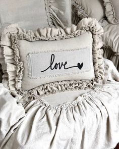 a pillow with the word love on it sitting on top of a bed covered in ruffled