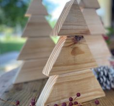 three wooden christmas trees sitting on top of a table next to pine cones and berries