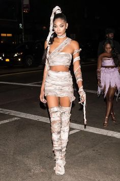 a woman walking across a street wearing thigh high boots and a dress with cutouts on it